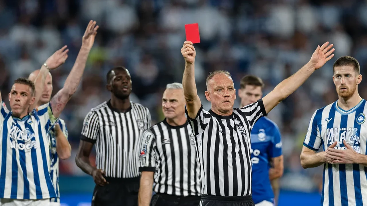Um jogador sentado sozinho no banco do estádio, de cabeça baixa, com o relvado desfocado por trás
