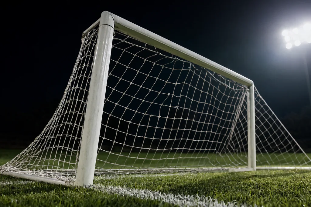 Estádio de futebol vazio à noite com projetores acesos sobre relvado escuro