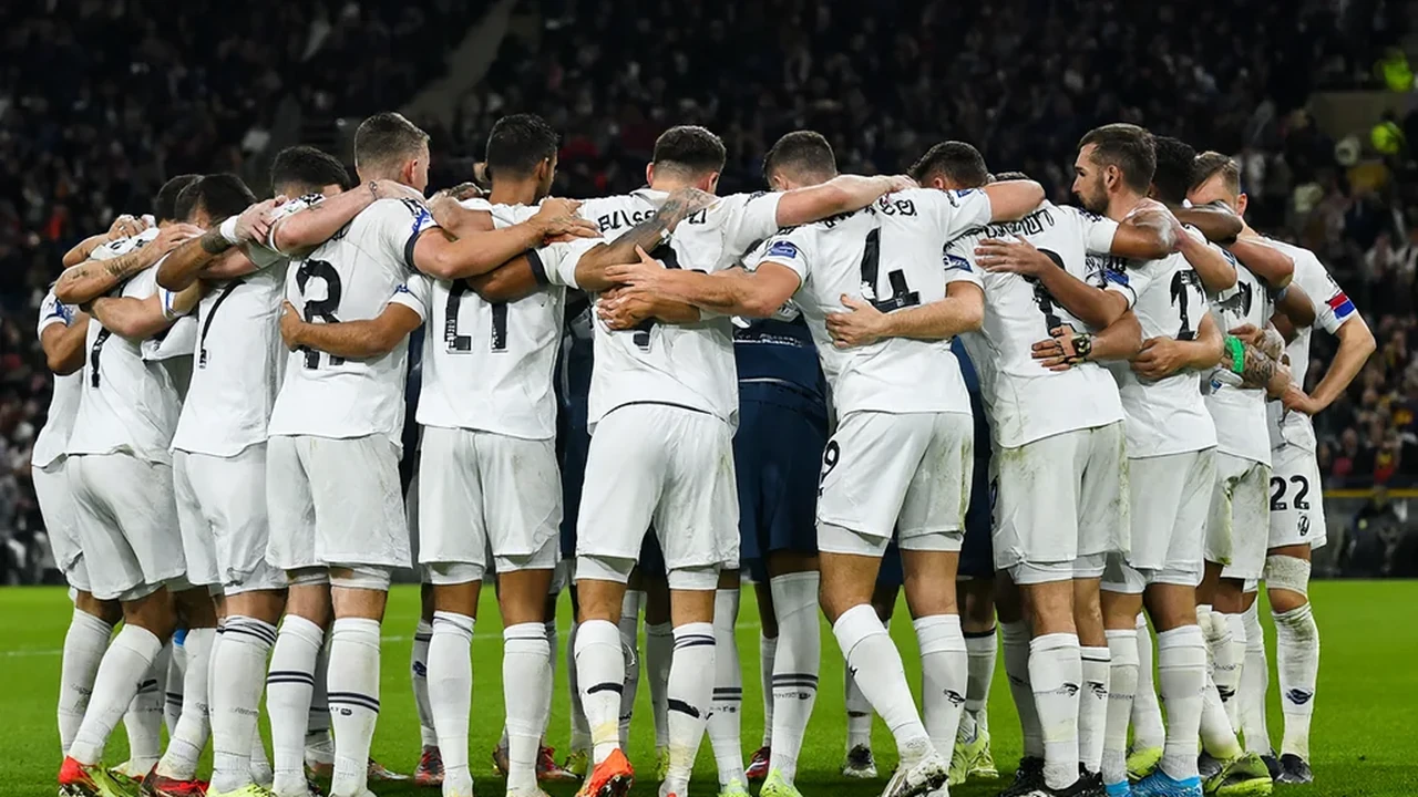 Dois jogadores disputam uma bola de cabeça num estádio cheio, com as bancadas desfocadas por trás